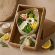 Bouquet of flowers in a brown box on a beige surface with lemon slices and herbs.
