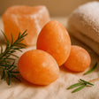 Three orange stones with rosemary leaves on a textured surface