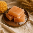 Three pink Himalayan salt blocks on a wooden plate with a sponge and fabric in the background.