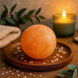 Orange Himalayan salt lamp on a wooden plate with a candle in the background