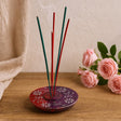 Incense stick holder with three incense sticks on a wooden surface next to pink roses.