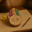 Decorative wooden hand with sun design on a textured surface with incense and flowers.