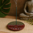Incense stick burning on a decorative holder with a Buddha statue and plant in the background