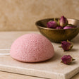 Pink konjac sponge on a beige surface with dried flowers in the background