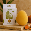 Konjac sponge with turmeric color next to its packaging on a wooden surface.