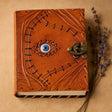 Brown leather notebook with eye design and metal clasp on a beige background