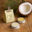 Coconut-based products including tins and a box on a wooden surface with a coconut half.