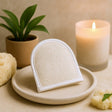 Heart-shaped bath sponge on a ceramic plate with a candle and plant in the background