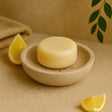 Bar of soap in a stone dish with lemon wedges on a beige background