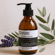 Brown bottle of Ancient Wisdom Muscle Ease Spa in a Bottle massage bath oil with lavender and eucalyptus leaves on a light background.