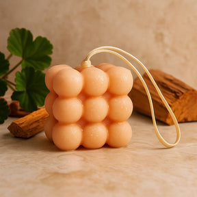 Cylindrical sponge with a string on a wooden surface with a plant and wood piece in the background