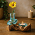 Decorative setup with a yellow flower in a glass vase on a wooden base, accompanied by a lit candle.