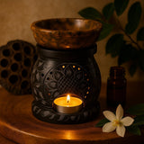 Aromatherapy lamp with a lit candle, surrounded by essential oil bottle and flower on a wooden surface.