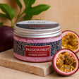 Jar of passion fruit shower souffle with a halved passion fruit on a wooden board.
