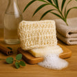 Natural soap bar with loofah on a wooden board with a glass bottle and cinnamon sticks in the background.