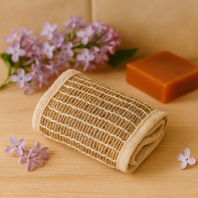 Knitted brown scrubber on a wooden surface with purple flowers and soap in the background