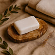 Bar of soap on a wooden dish with a towel and leaves in the background