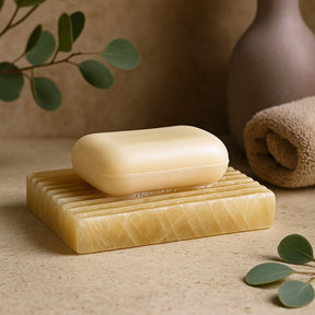 Bar of soap on a natural stone soap dish with green leaves and a vase in the background