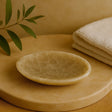 Beige ceramic dish on a wooden surface with a beige towel and green leaves in the background