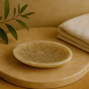 Beige ceramic dish on a wooden surface with a beige towel and green leaves in the background
