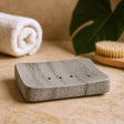 Gray stone soap dish on a wooden surface with a towel and brush in the background