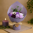 Bouquet of soap flowers wrapped in purple paper with a candle and greenery on a beige background
