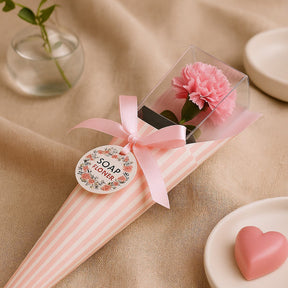 Pink soap flower in a clear packaging with a ribbon on a beige fabric background