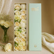 Floral arrangement in a box with 'MESQUIL BLOUQUET' branding, next to a vase of flowers on a beige surface.