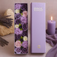 Box of purple and white flowers with a lit candle and lavender on a beige background