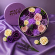 Round box of flowers with 'Merci Bouquet' branding on a purple fabric background