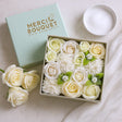 Box of white and green roses with 'Merci Bouquet' branding on a light background