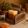 Square soap in a wooden holder with decorative elements on a textured surface.