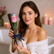 Woman holding a gift box with a pink rose inside, standing in a bathroom.