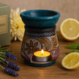 Decorative wax warmer with a lit candle on a wooden surface with lemons and lavender.