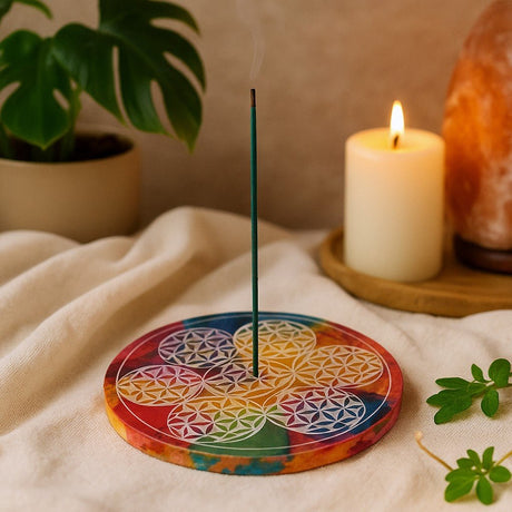 Colorful circular incense holder with a lit candle and plant in the background