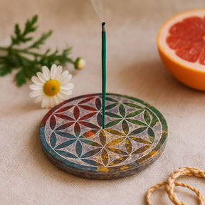 Incense burner with a smoking incense stick on a decorative mat, next to a daisy and half a grapefruit.