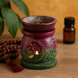 Decorative oil burner with Om symbol on a wooden surface with a bottle and beads in the background.