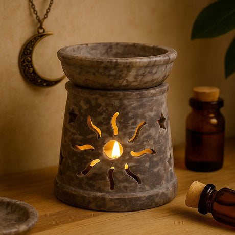 Decorative stone oil burner with a lit candle on a wooden surface, surrounded by bottles and a moon pendant.