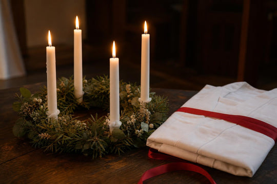 A wreath of lit candles beside a folded white robe and red ribbon, recalling the traditional Lucia crown