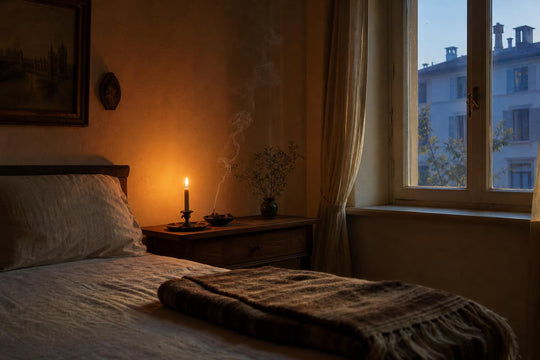 A candle and incense burning quietly on a bedside table before dawn, the room lit only by flame