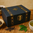 Decorative black box with brass accents on a bamboo mat with tea leaves and a cup.