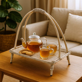 Tea set with a teapot, cups, and cookies on a woven tray in a cozy living room.
