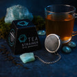 Tea strainer with gemstone next to a cup of tea on a dark background