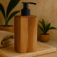 Wooden soap dispenser with black pump on a wooden surface with plants in the background