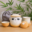 Cute panda-shaped ceramic tea set with a gray drawstring bag on a wooden surface.