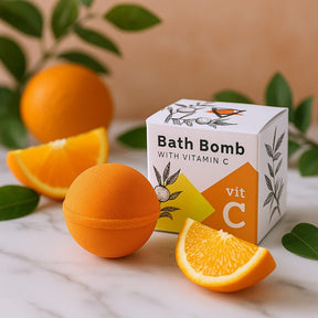 Orange bath bomb with vitamin C next to its packaging on a marble surface with oranges and leaves.