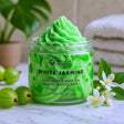 Green whipped soap in a jar with 'Ancient Wisdom' branding, surrounded by gooseberries and white flowers.
