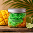 Jar of Mango & Lime scented whipped soap with a mango and lime on a wooden surface.